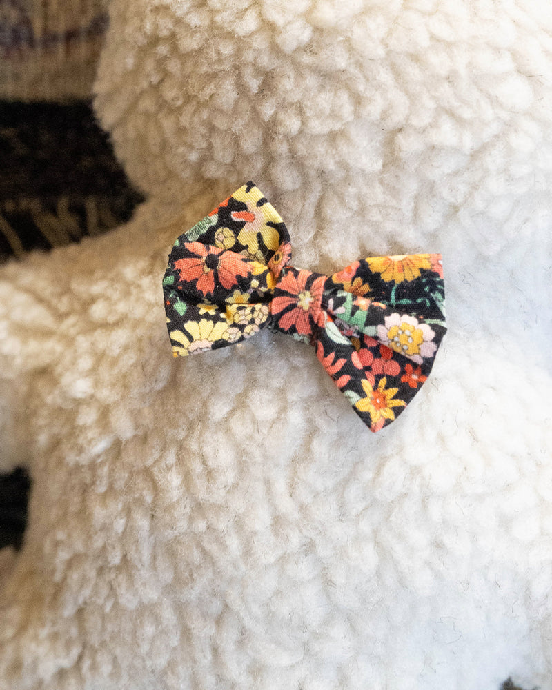 Plush Dog Toy filled with 100% organic lavender to help calm your pet. Wearing a black floral bowtie. Designed to give back 100%.