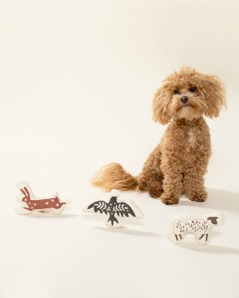 Three cotton canvas folk animals. A red/brown bunny, white sheep, and a grey bird with a leaf pattern. Featured with a poodle mix dog.