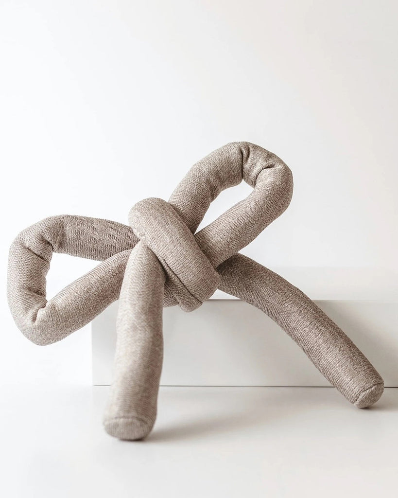 Tan NOUNOU by Lambwolf Collective. A long versatile toy tied into a bow.